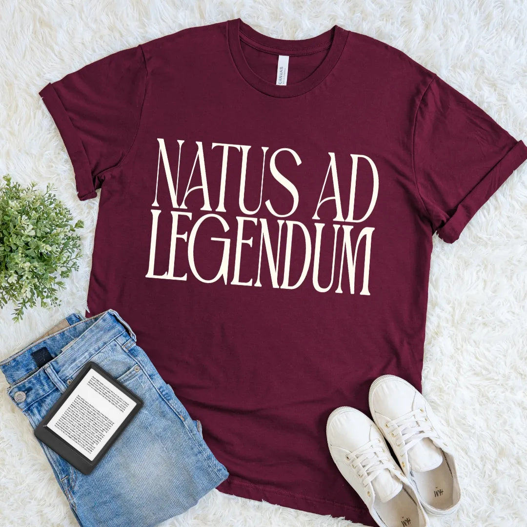Maroon red reader shirt featuring Natus ad Legendum in oversized cream serif typography.
