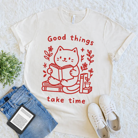 “Good things take time” quote with bookish cat design on cream shirt