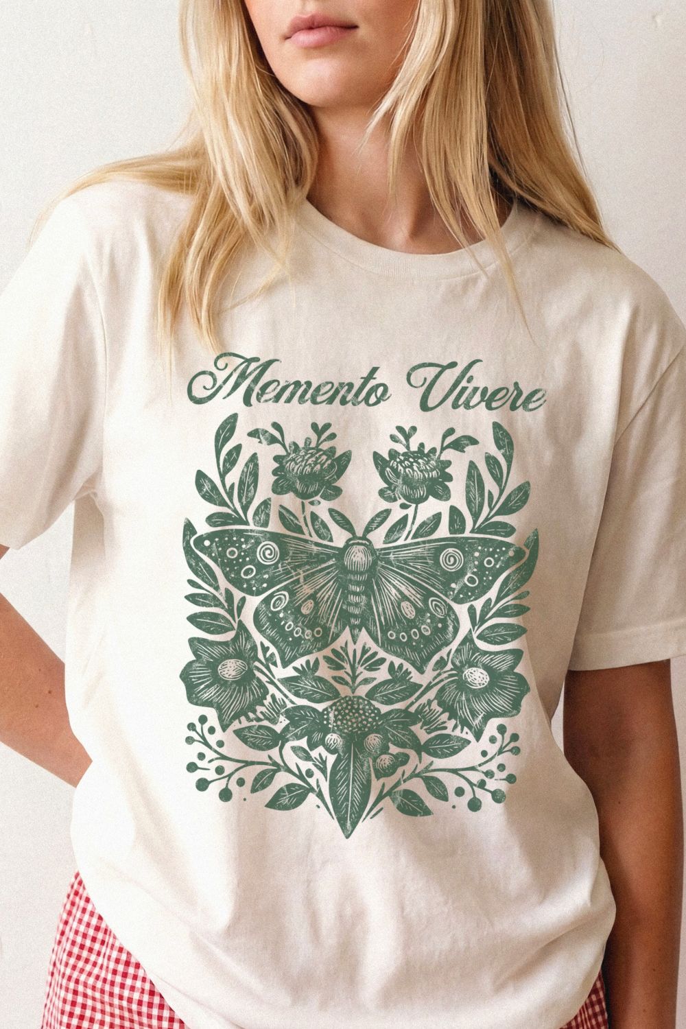 Woman wearing a natural beige botanical t-shirt with a green butterfly design and 'Memento Vivere' text styled in relaxed academia outfit