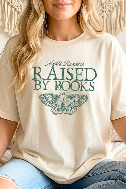 Woman wearing a beige reader t-shirt with 'Raised by Books' text and butterfly graphic styled with jeans for cozy bookish outfit