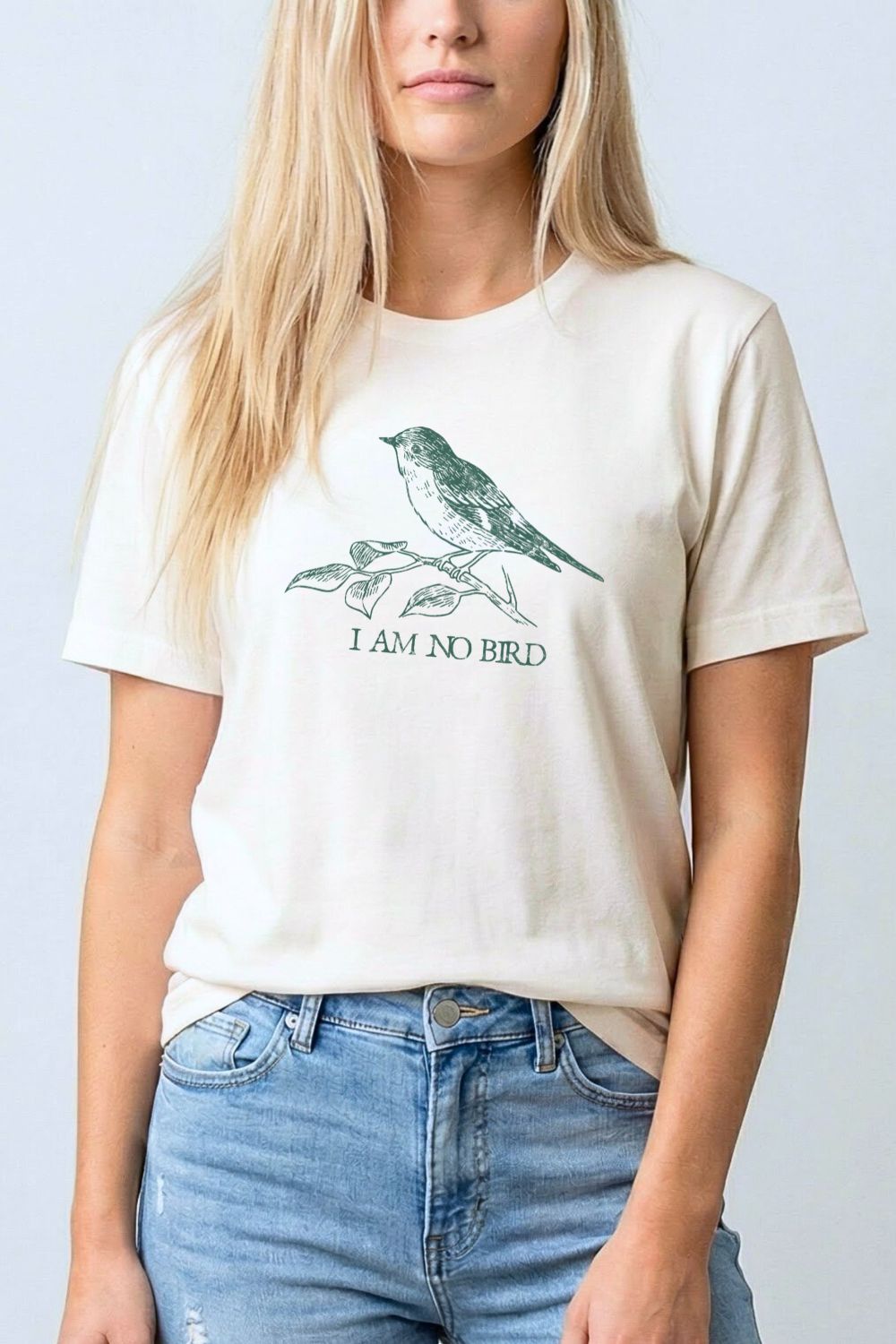 woman wearing a natural beige  t-shirt with a vintage bird design and "I am no bird" quote, style with jeans for relaxed soft academia outfit