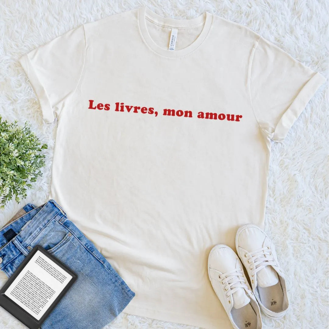 Natural Les Livres, Mon Amour French book lover T-shirt with deep red serif lettering, styled with jeans, white sneakers, and an e-reader