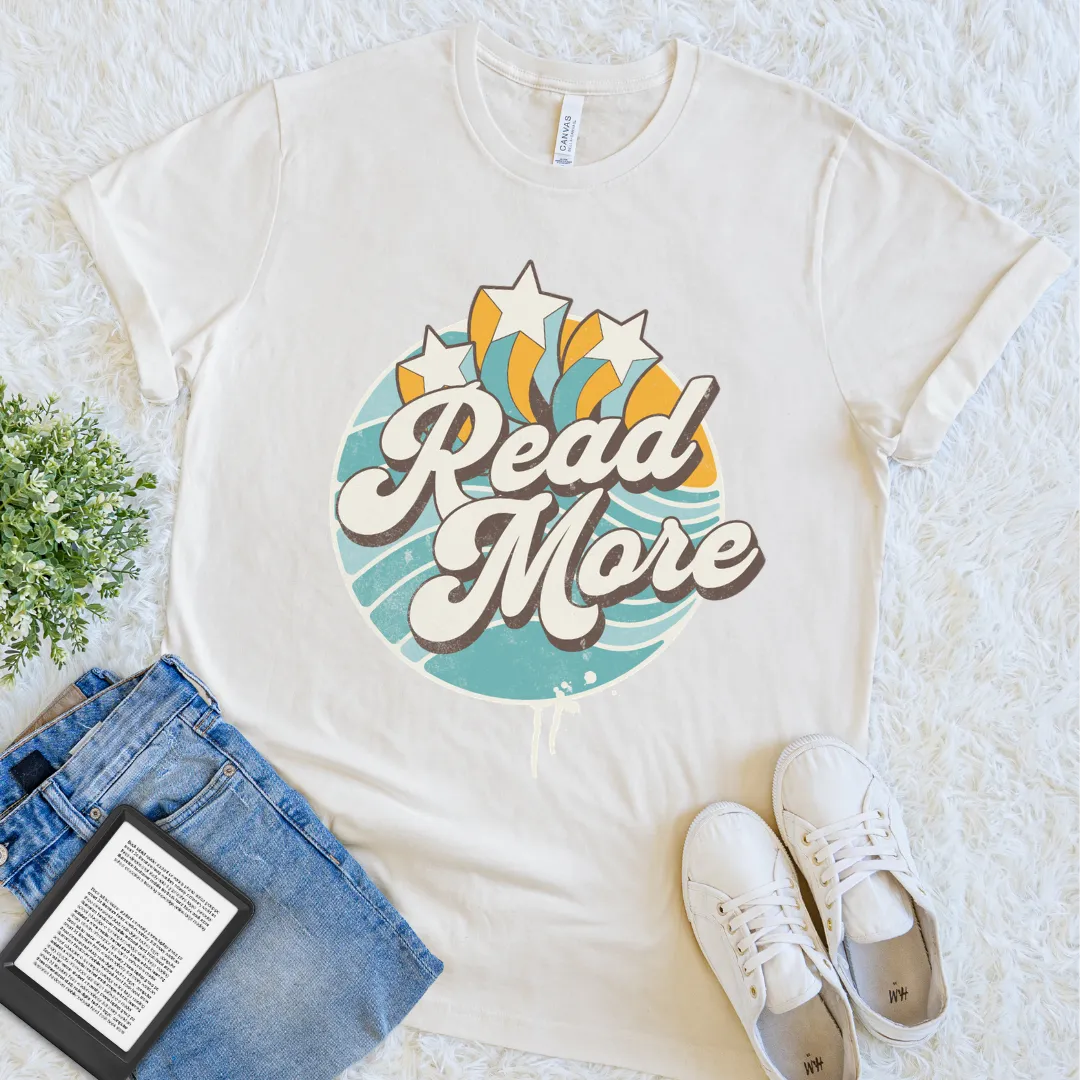 Natural “Read More” T-shirt with colorful retro typography, star accents, and a vintage burst design, a cheerful book lover graphic tee for readers.