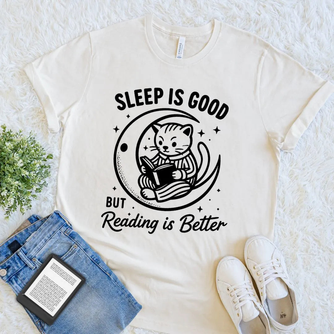 Cream reader shirt featuring a cat reading a book on a crescent moon with stars and playful typography.
