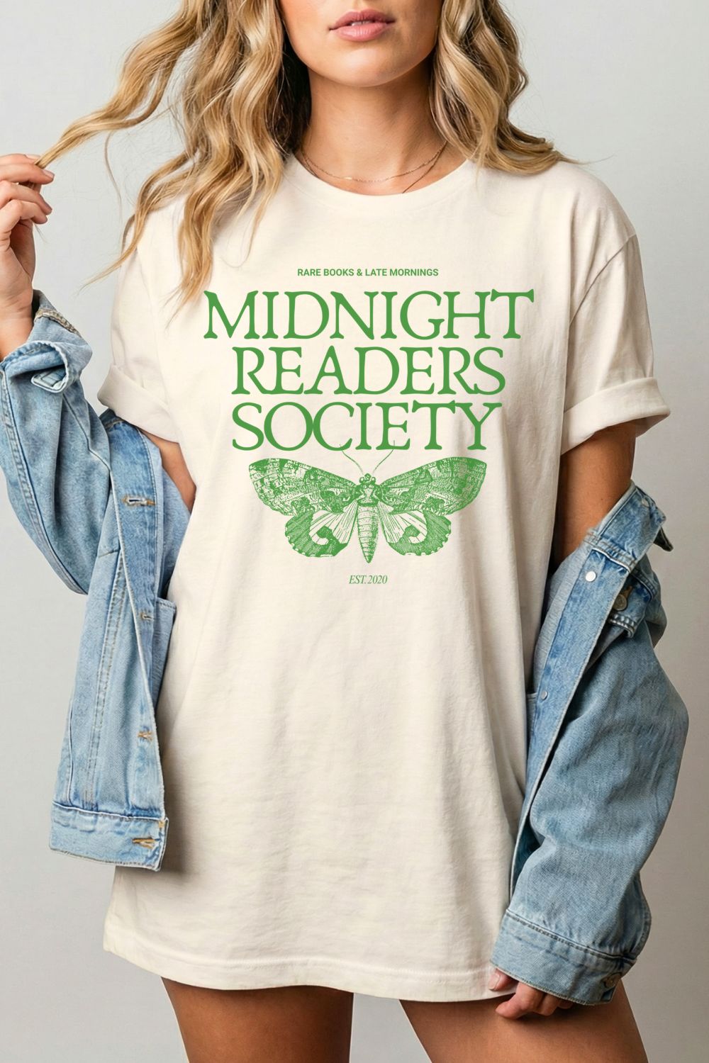 woman wearing a 'Midnight Readers Society' bookish shirt with a green vintage  moth graphic on a plain background