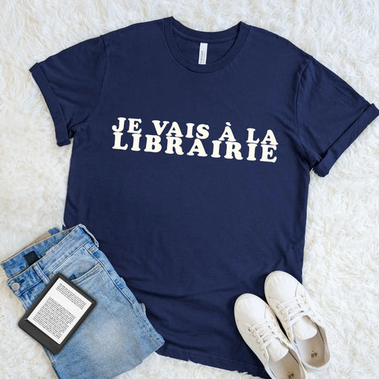 Navy Je Vais à La Librairie French bookstore T-shirt with bold cream retro lettering, styled with jeans, white sneakers, and an e-reader