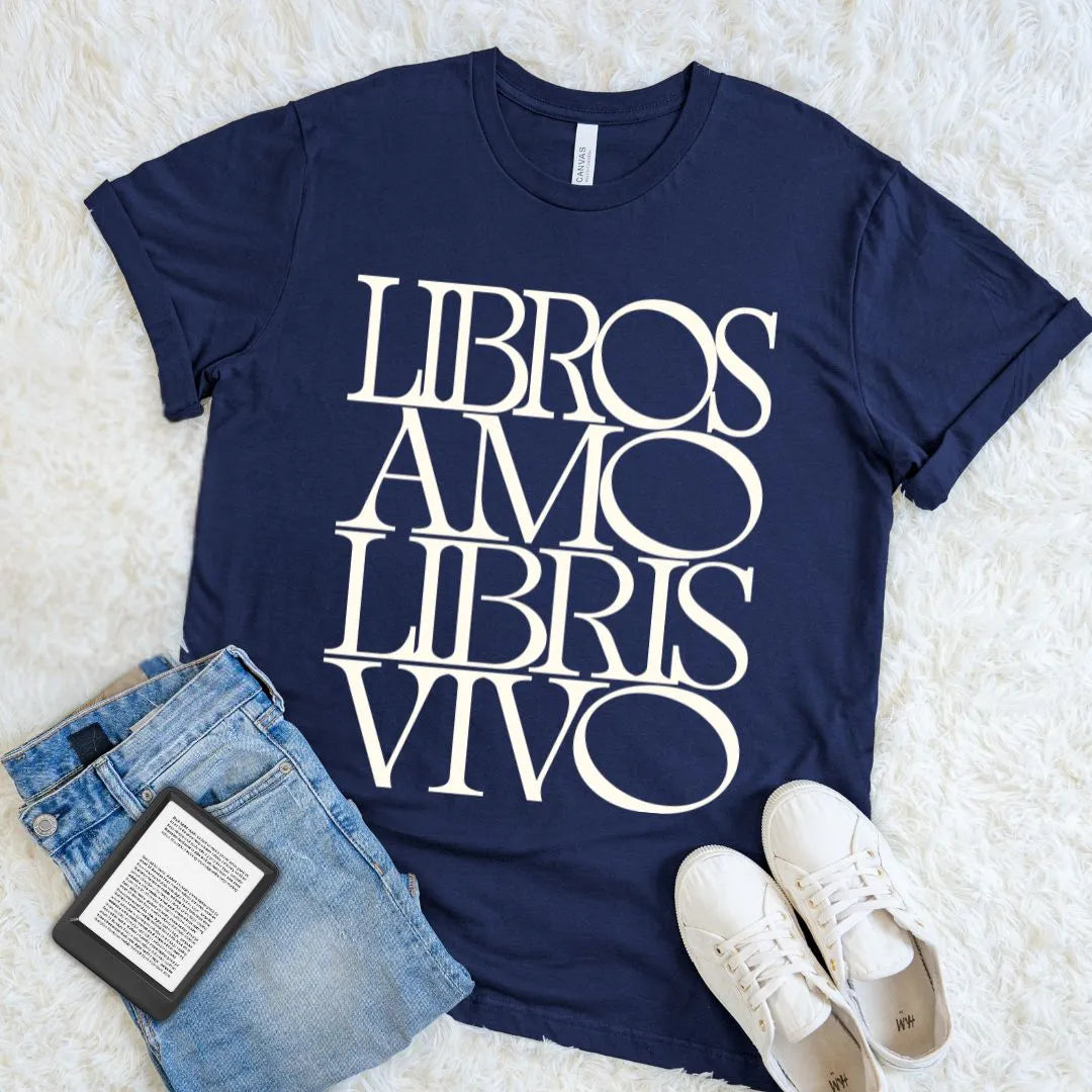 Navy Libros Amo Libris Vivo Latin book lover T-shirt styled with denim, white sneakers, and an e-reader on a soft white rug