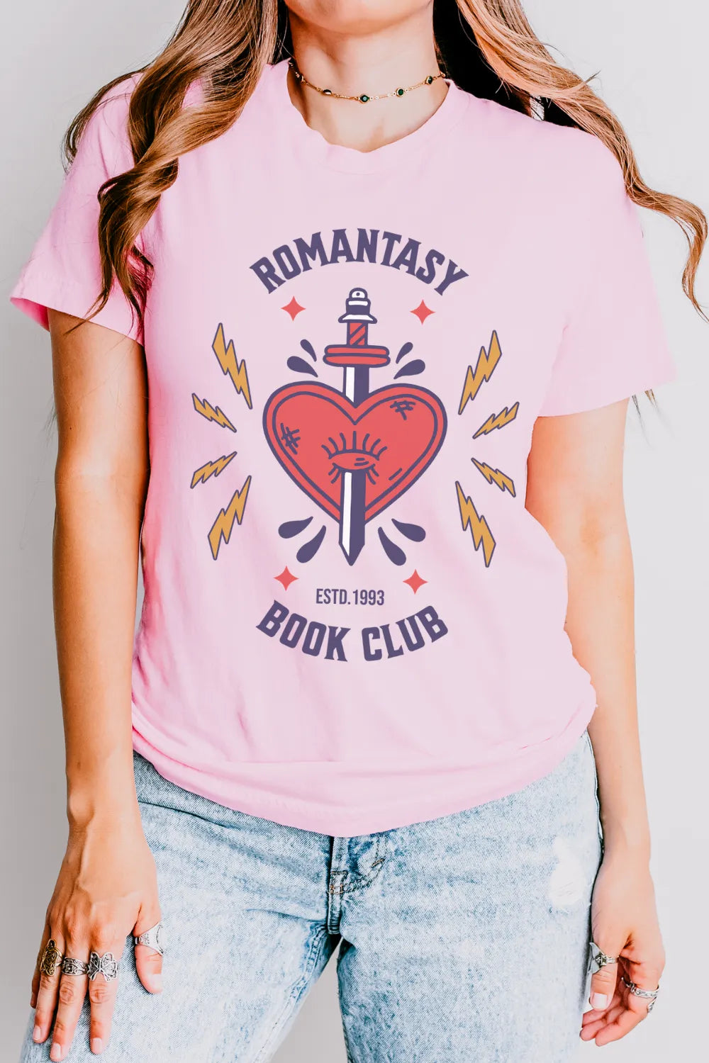 woman wearing pink vintage-style book lover T-shirt with red heart and sword design, text reads “Romantasy Book Club”