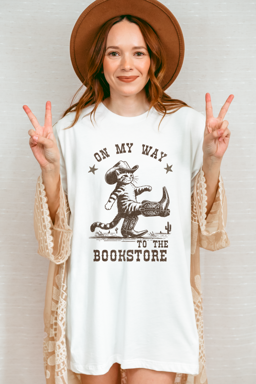 woman wearing cream T-shirt with cowboy cat and “On My Way to the Bookstore” quote