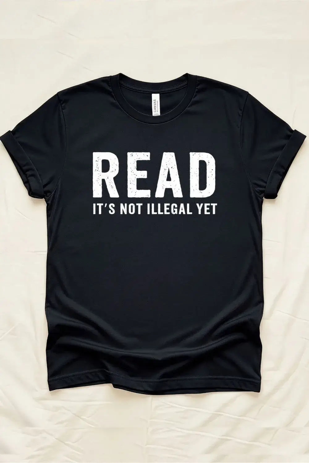 Black graphic t-shirt with bold white distressed text reading “Read – It’s Not Illegal Yet” in a minimalist statement style.