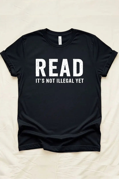 Black graphic t-shirt with bold white distressed text reading “Read – It’s Not Illegal Yet” in a minimalist statement style.