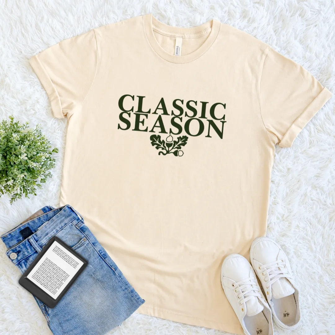 Soft Cream Classic Season bookish T-shirt with dark vintage serif typography, oak leaves and acorns, a cozy fall literary tee for readers and rereaders.