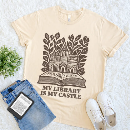 Soft cream book lover T-shirt with castle illustration rising from open book design with "my castle is my library" text