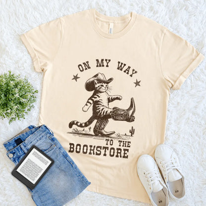 Cream T-shirt with cowboy cat wearing boots and hat, text reads “On my way to the bookstore”