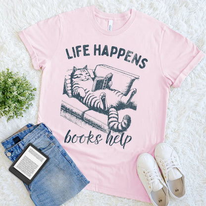cat reading on a couch illustration on “Life Happens Books Help” literary tee with vintage vibe in soft pink