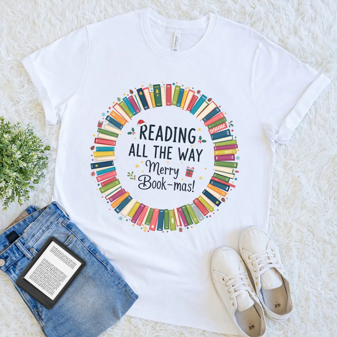 “Reading All the Way – Merry Bookmas” text with colorful book stack design on white t-shirt
