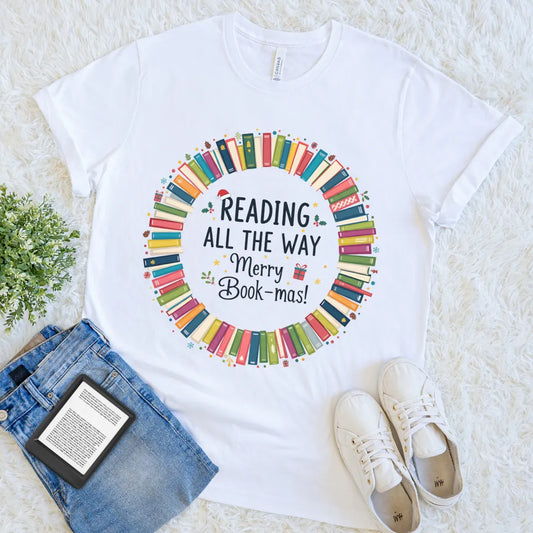 “Reading All the Way – Merry Bookmas” text with colorful book stack design on white t-shirt