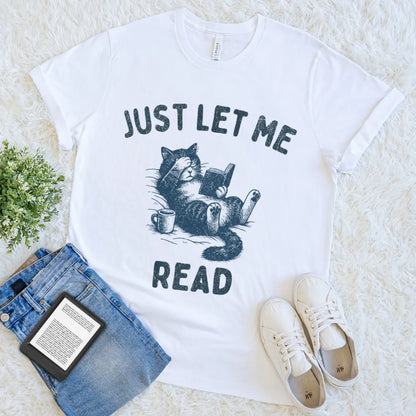 Flat lay of white reader tee with book, coffee, and snuggly cat graphic