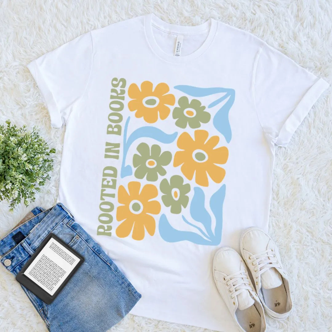 White soft cotton  t-shirt featuring a retro floral design in mustard, sage, and light blue with the  ‘Rooted in Books’ quote