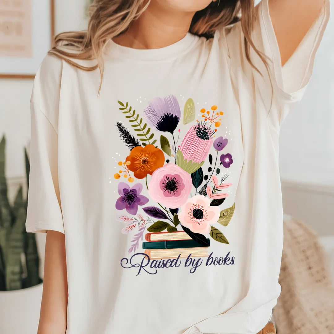 Woman wearing a cozy floral tee for book lovers with hand-drawn bouquet illustration and “Raised by books” quote