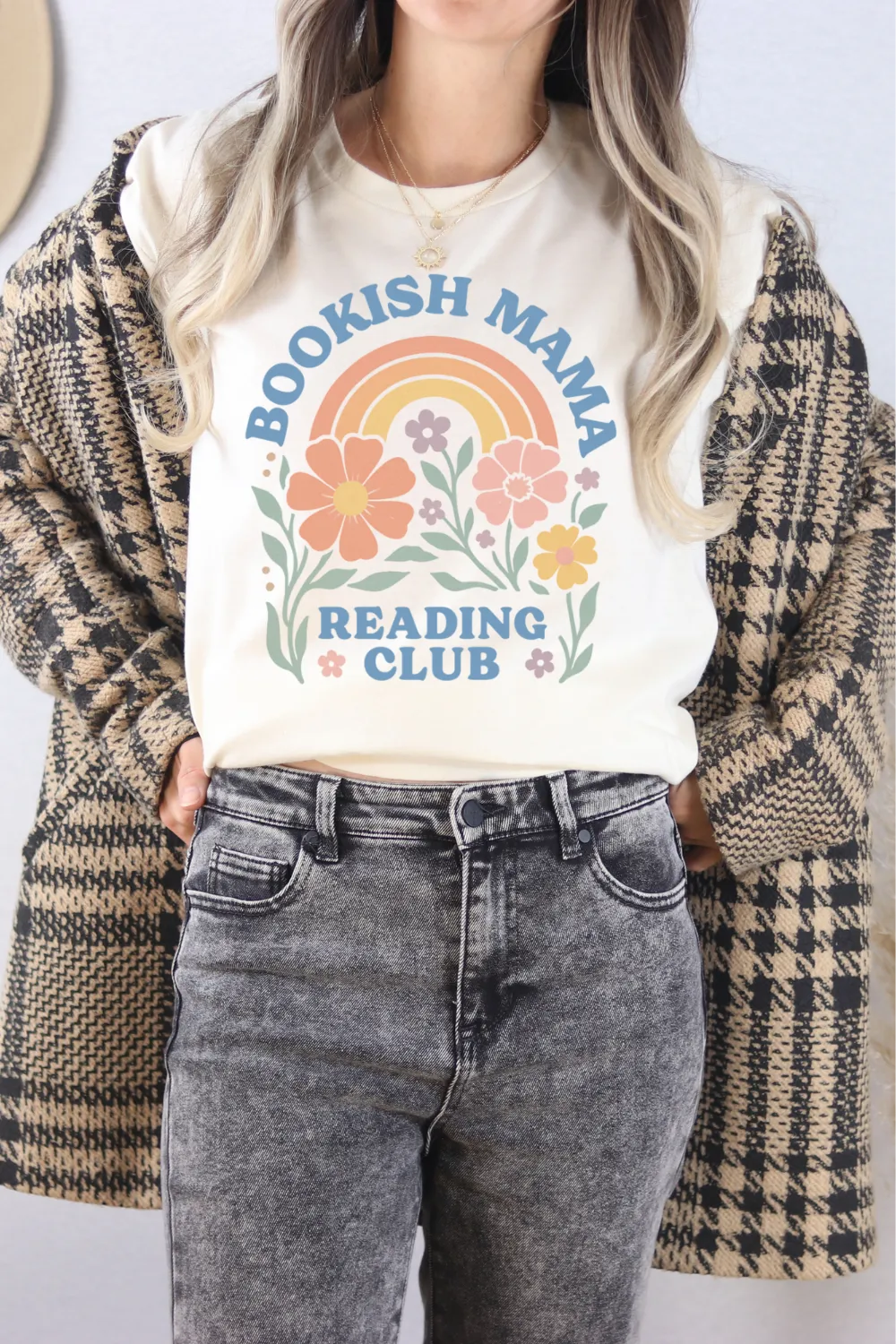 woman wearing cream T-shirt with pastel rainbow, flowers, and “Bookish Mama Reading Club” text