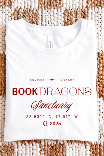A white t-shirt with red typography reading “Book Dragons Sanctuary,” inspired by ancient libraries and bookish fantasy aesthetics folded on textile background