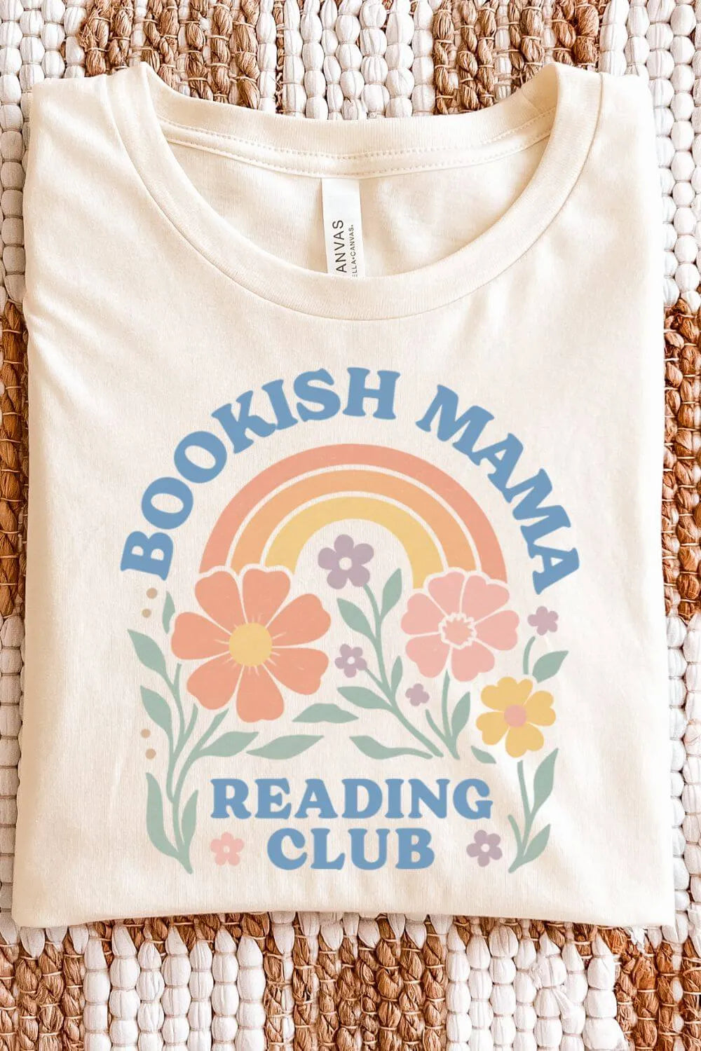 soft cotton natural beige graphic t-shirt with pastel floral illustrations, a rainbow, and the text “Bookish Mama Reading Club” in a cozy bookish style, folded on textile surface