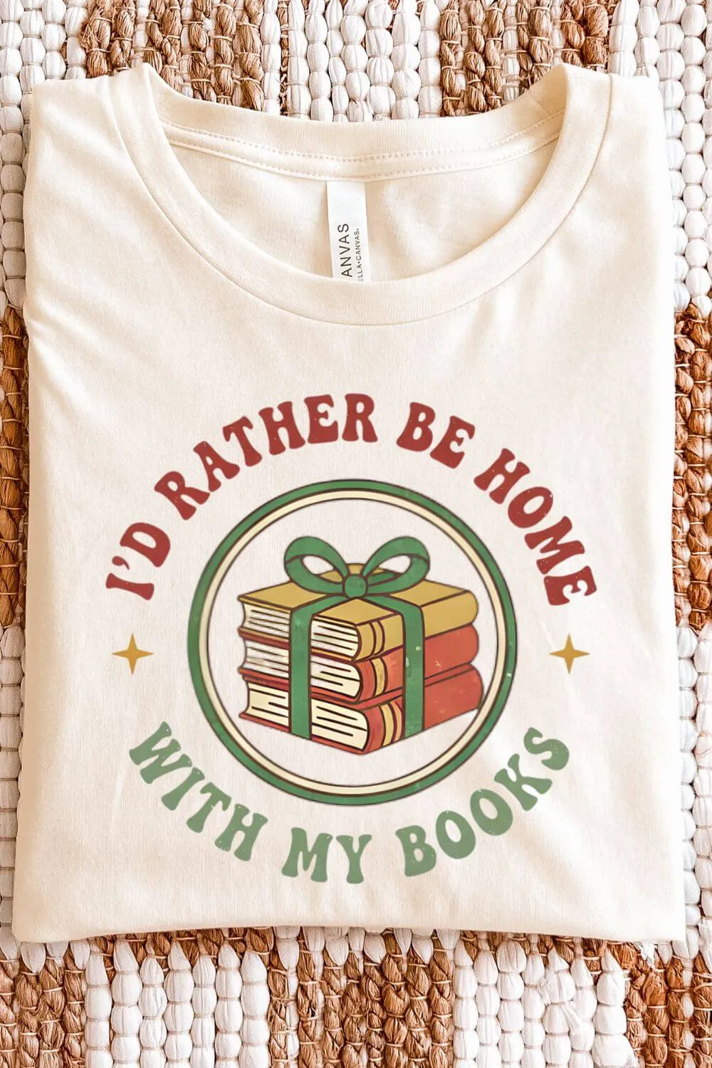 Soft cotton natural beige  retro graphic t-shirt featuring a stack of books tied with a green ribbon and the phrase “I’d Rather Be Home With My Books” in vintage red and green lettering.
