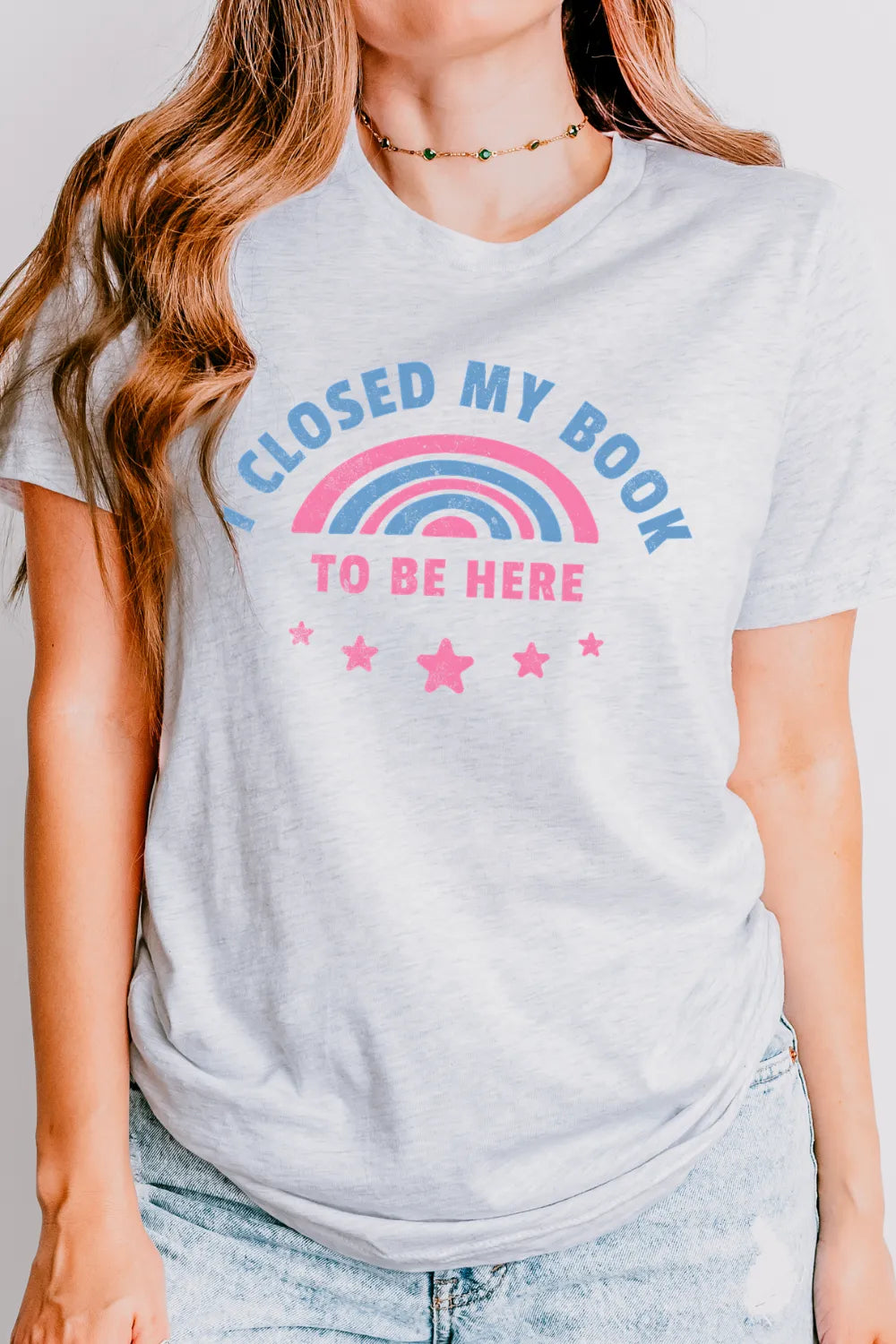 woman wearing soft cotton T-shirt with pink and blue rainbow and bold text saying “I closed my book to be here”