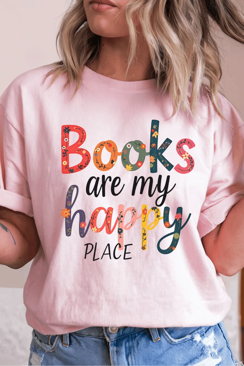woman wearing soft pink T-shirt with colorful floral text reading “Books are my happy place”