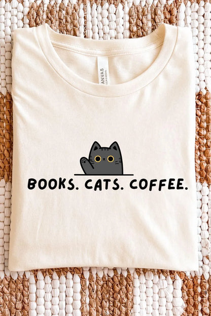 A cream-colored soft cotton  t-shirt featuring a small gray cat illustration peeking over a line with the words ‘Books. Cats. Coffee.’ in simple black text.