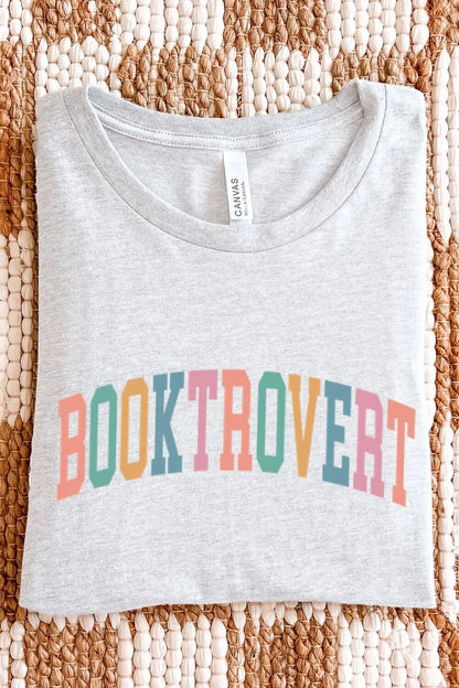 A light ash gray t-shirt featuring the word “Booktrovert” in colorful retro collegiate-style pastel lettering, designed for book lovers and introverts, folded on textile surface.