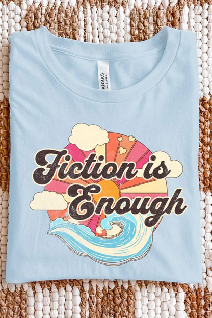 A folded light blue retro-style graphic t-shirt with colorful sunset and ocean wave artwork and bold vintage lettering that reads “Fiction Is Enough” for groovy aesthetic outfit