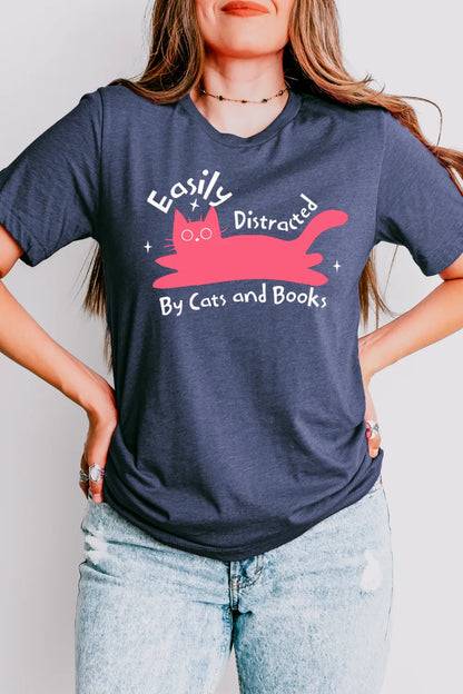 woman wearing a heather navy bookish t-shirt with pink cartoon cat and playful “easily distracted by cats and books” quote