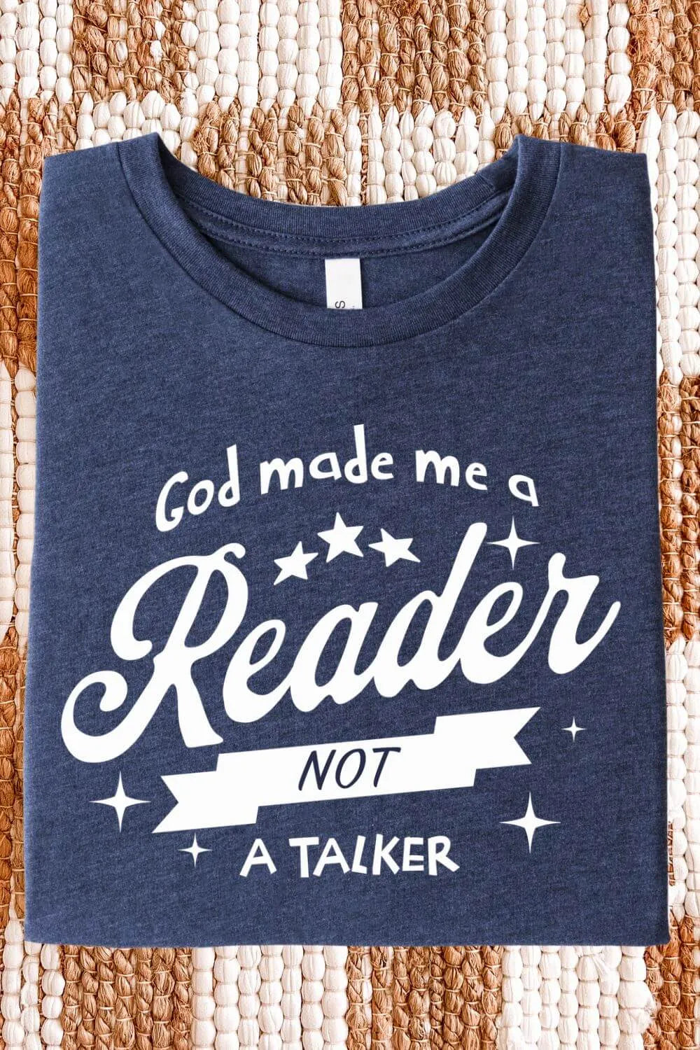 A soft heather navy blue t-shirt with white vintage-style text reading “God Made Me a Reader Not a Talker,” folded on textile surface