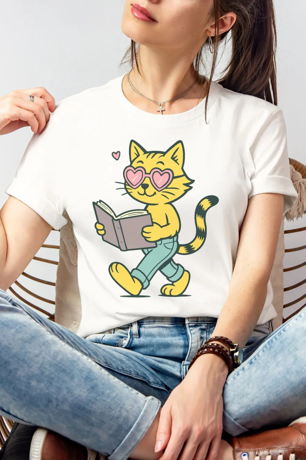 White soft cotton t-shirt worn by a woman featuring a cute illustrated yellow cat wearing heart-shaped glasses and walking while reading a book