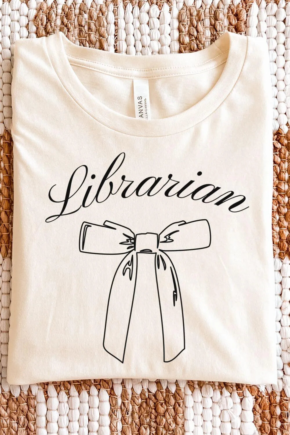 A cream-colored minimalist t-shirt with the word “Librarian” in elegant script and a simple bow illustration, styled in a light academia aesthetic