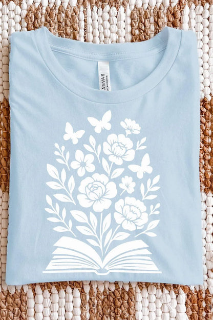 A light blue soft cotton  t-shirt with a white illustration of an open book blooming with flowers and butterflies, designed in a soft, nature-inspired bookish style.