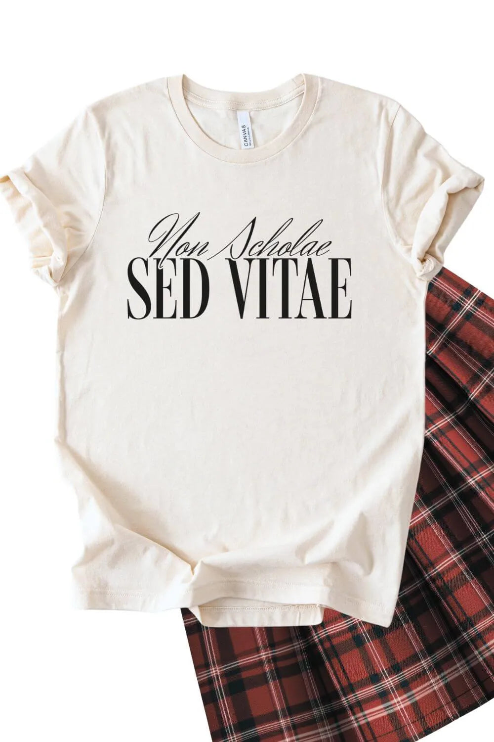 A soft cotton natural beige t-shirt featuring the Latin phrase “Non Scholae Sed Vitae” in elegant black serif typography, styled with a plaid skirt for a dark academia aesthetic