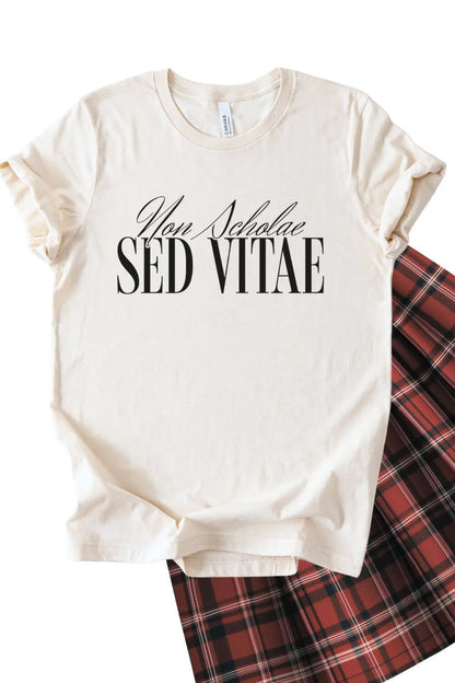 A soft cotton natural beige t-shirt featuring the Latin phrase “Non Scholae Sed Vitae” in elegant black serif typography, styled with a plaid skirt for a dark academia aesthetic