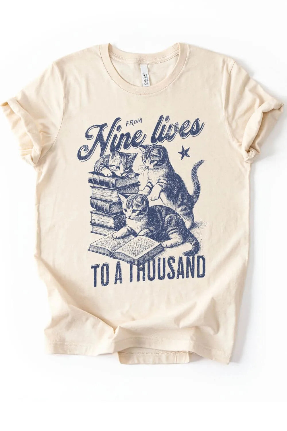 soft cotton natural beige  graphic t-shirt with a vintage illustration of kittens reading books and the text “From Nine Lives to a Thousand” in a cozy bookish style.